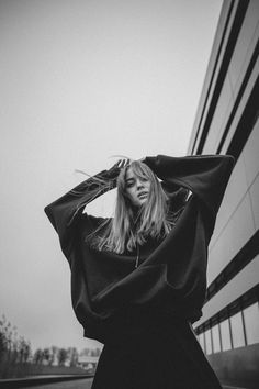 a woman standing in front of a tall building with her hands on her head and looking at the camera