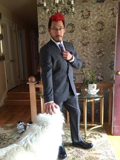 a man in a suit and tie standing next to a white dog on a rug