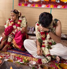 two people sitting on the ground with flowers in their hair and garlands around them