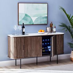 a wooden cabinet with wine bottles and glasses on it in front of a blue wall