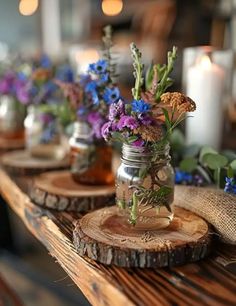 mason jar filled with purple and blue flowers sitting on top of a wooden table next to candles