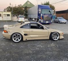 a tan sports car parked in a parking lot next to a semi - truck and other vehicles