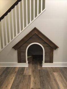 a dog house under the stairs is made out of wood and has an arched door