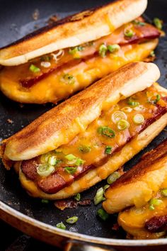 two hot dogs with cheese and onions in a frying pan