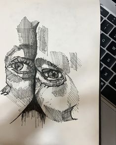 a drawing of two people's faces on top of a piece of paper next to a laptop computer