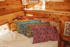 there are many pillows on the bed in this cabin room with wood walls and windows