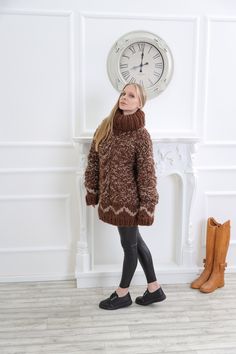 a girl standing in front of a clock wearing a brown sweater and black leggings