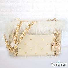 a white purse with gold chains and pearls on the front, sitting against a white brick wall