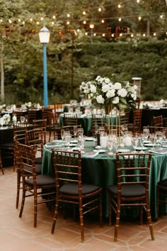 an outdoor wedding reception set up with green linens and white flowers in tall vases