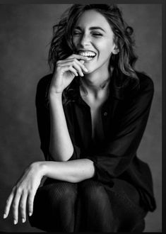 a black and white photo of a woman smiling with her hands on her chins