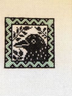 a cross stitch picture with a black bird on it's back and green border