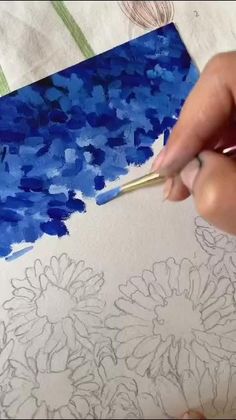 someone is drawing flowers on paper with blue ink and watercolor pencils in their hands