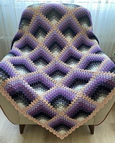 a crocheted blanket sitting on top of a wooden chair next to a window