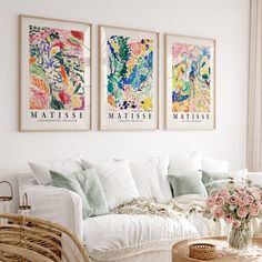 three paintings hang on the wall above a white couch and coffee table with pink flowers