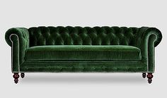 a green velvet couch with wooden legs and buttons on the back, in front of a gray background