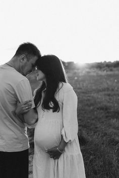 a pregnant woman standing next to a man in a field