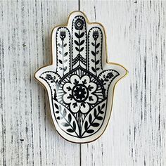 a decorated hamsa hanging on a white wooden wall with black and white flowers in the middle