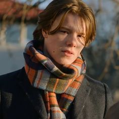 the young man is wearing a plaid scarf and looking off into the distance with his hand on his hip