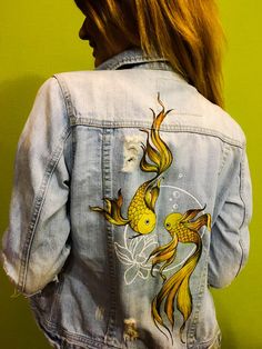 a woman wearing a jean jacket with gold fish painted on the front and back of it