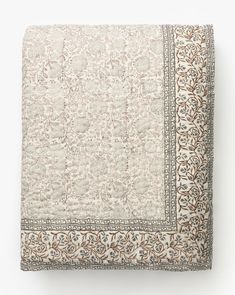 a white and brown quilted bed spread with an intricate design on the bottom corner