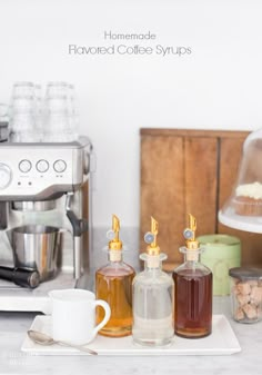 three bottles of liquid sitting on top of a white plate next to a coffee maker