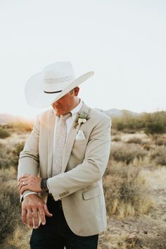 a man wearing a white hat and suit in the middle of an open desert area