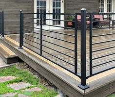 a wooden deck with metal railings and chairs on the front lawn area next to a house