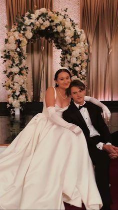 a bride and groom posing for a photo in front of a floral arch at their wedding