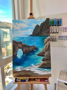 an easel with some paint on it in front of a window that has a view of the ocean