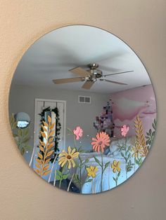 a mirror with flowers painted on it in the middle of a room that has a ceiling fan