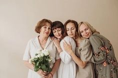 three women are hugging each other and one woman is holding a bouquet in her hands