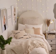 a bed with white sheets and pillows in a bedroom next to a potted plant