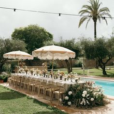 an outdoor dining area with tables and umbrellas next to a pool in the grass