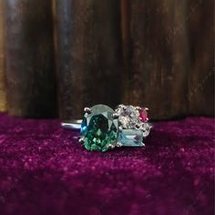 an oval cut green and white diamond ring on purple velvet with wood in the background