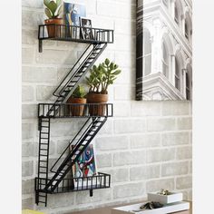 a black metal shelf with plants and books on it next to a white brick wall