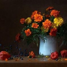 a white vase filled with lots of orange and yellow flowers