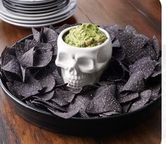 a plate with chips and guacamole in it on a wooden table next to stacks of plates