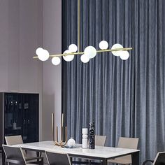 a modern dining room table and chairs with lights hanging from the ceiling above it in front of a curtained window