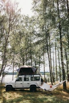 a white jeep parked in the woods with a hammock hanging from it's roof