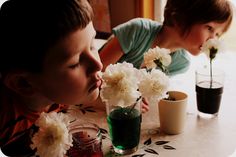 two young children sitting at a table with flowers in vases and cups on the table