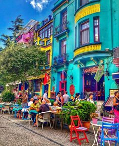 people are sitting at tables in front of colorful buildings