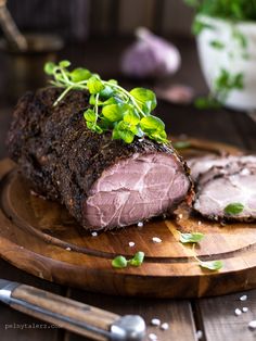 a piece of meat sitting on top of a wooden cutting board next to some greens