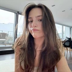 a woman with long brown hair sitting in front of a glass wall looking at the camera