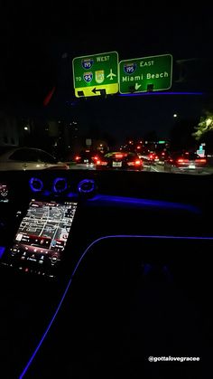 the interior of a car at night with blue lights and street signs in the background