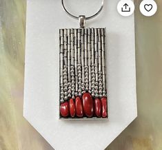 a silver and red necklace on a white piece of paper with bamboo sticks in the background