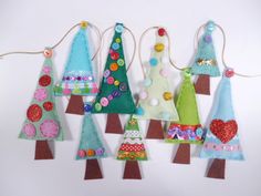 several felt christmas trees hanging from strings on a white wall with buttons and sequins