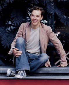 a man sitting on top of a red box next to plants and trees in the background