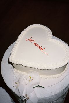 a heart shaped cake with the words just married written on it and flowers in front