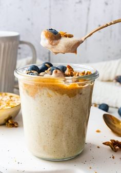 a spoonful of granola with blueberries and walnuts is being lifted from a glass jar