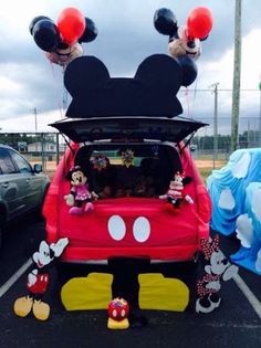 mickey and minnie mouse balloons are on top of the back of a car in a parking lot